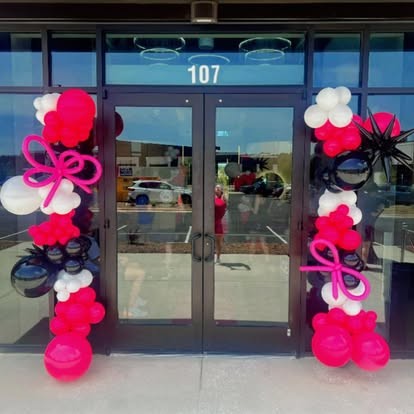 Pink, white and black balloon columns with ribbon bows framing a business entrance