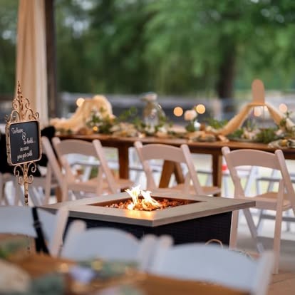 Fire pit lounge area beside long farm tables with candles and greenery at dusk