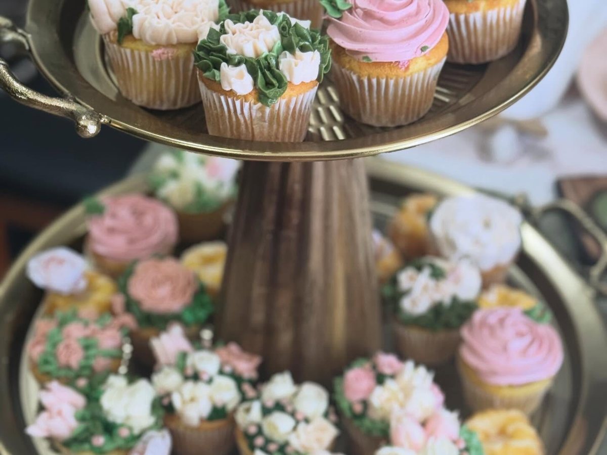 Two-tier gold stand of floral buttercream cupcakes in blush, white and green