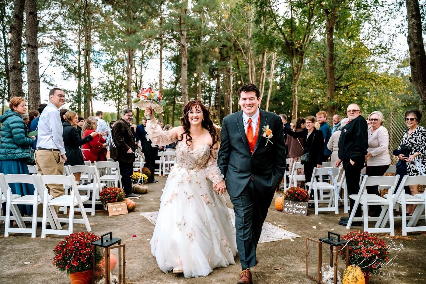 Bride raising her bouquet as the couple walks back up the aisle past cheering guests (photographer watermark shown)